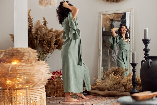 Фото Красивая женщина в оформленной комнате в стиле бали смотрит на себя в зеркало