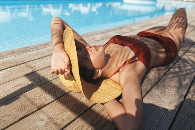 사진 여름 휴가를 즐기는 수영장에서 종려나무 아래 나무 부두에서 휴식을 취하는 모자를 쓴 아름다운 여성