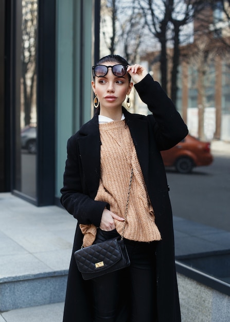Фото Красивая женщина в солнечных очках и черном длинном пальто на улице.