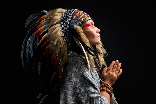 Beautiful woman in Indian hat with feathers, accessories Bohemians and Boho, she is looking up, praying. isolated black wall