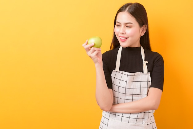 Beautiful woman is holding apple on yellow background