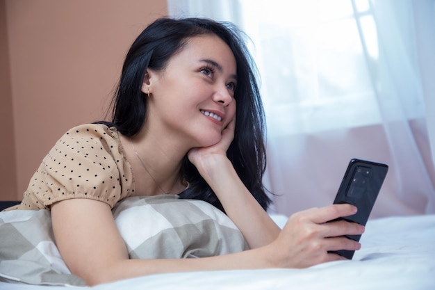 Beautiful woman is imagining on the bed while holding a cell phone