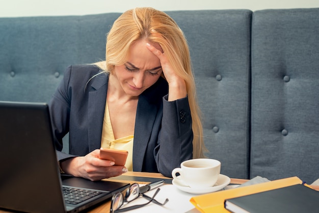 A beautiful woman is looking at smart phone with feeling sad at modern cafe.