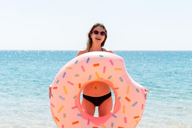 Beautiful woman is playing with donut rubber ring on the beach at the sea background