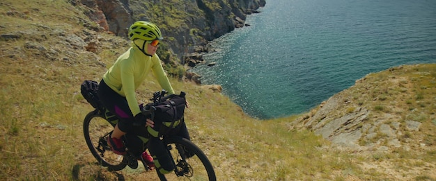 The beautiful woman is ride on top of a hill with the sea in the background near the canyon The sporty girl travels on a bicycle with bikepacking bags The traveler journey on touring bicycle