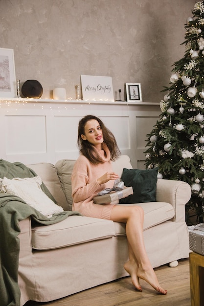 A beautiful woman is sitting on the sofa . New Year's and Christmas