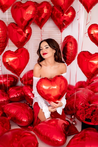 Красивая женщина сидит в окружении красных шаров в форме сердца девушка в белой рубашке концепция Дня святого Валентина