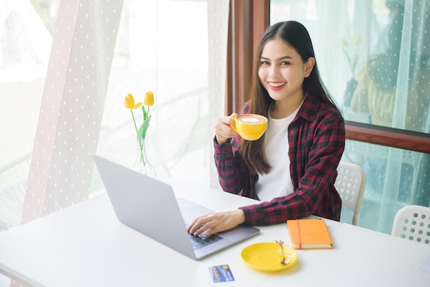 美しい女性はコーヒーショップでラップトップコンピューターで働いています。