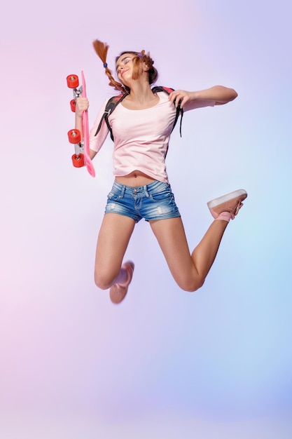 Beautiful woman jumping with longboard on pink background