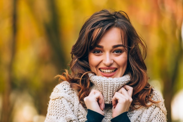 Beautiful woman in a knitted cardigan touches collar with hands Park background Autumn landscape