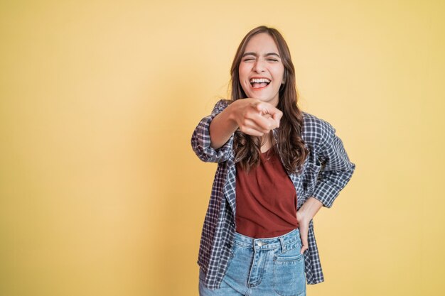 Beautiful woman laughing with hand gesture pointing at camera while standing with copyspace