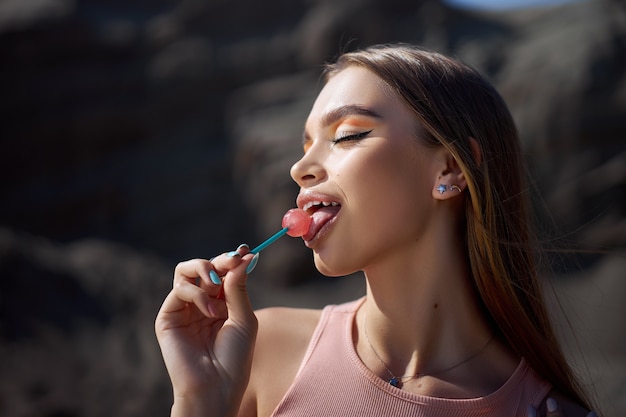 Photo beautiful woman licking a lollipop close-up. red shadows on the eyes of a girl, professional makeup, natural cosmetics