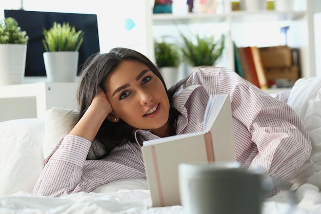 Beautiful woman lies in bed and reads book