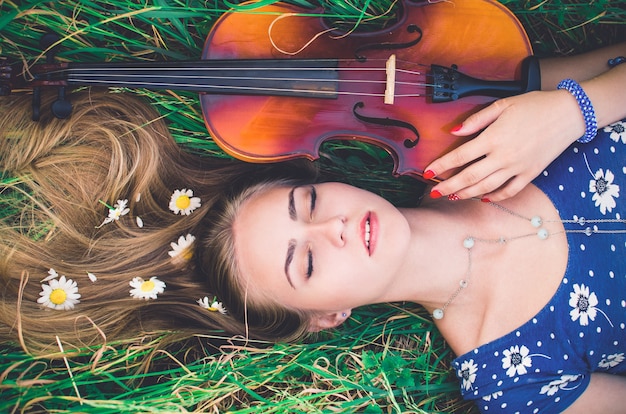 Photo beautiful woman lies in tall grass, with violin