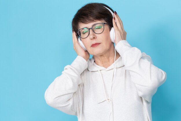 Beautiful woman listening to music in big headphone on blue wall