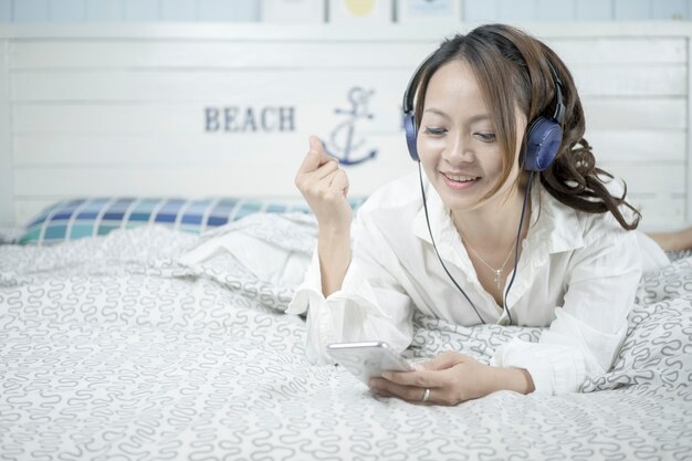 Beautiful woman listening music in headphones on her bed.