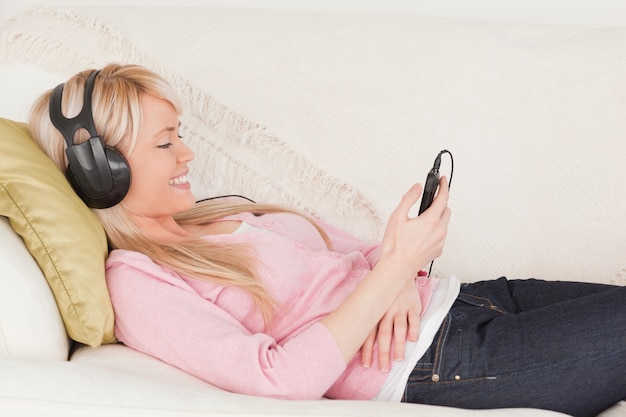 Beautiful woman listening to music on her headphones while lying on a sofa
