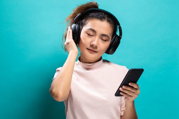 青い背景にスマートフォンを使って音楽を聴いている美しい女性