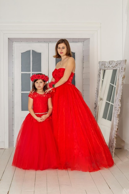 Photo a beautiful woman in a long pink dress in a hall with flowers is photographed with her daughter with a wreath of flowers on her head the girls are cute spring photosession family