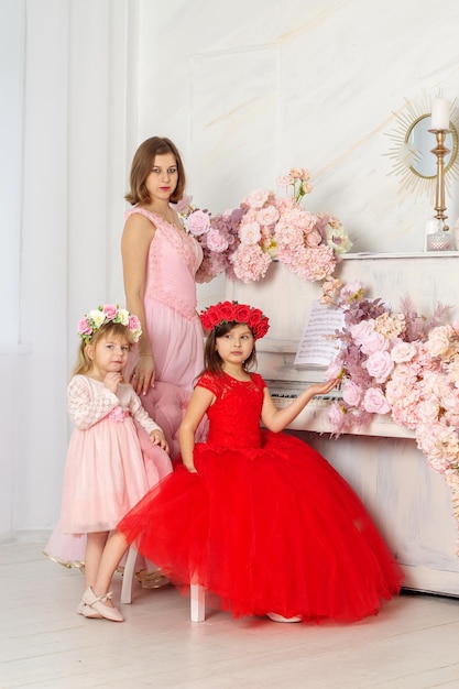 A beautiful woman in a long pink dress in a hall with flowers is photographed with her daughters who have wreaths of flowers on their heads The girls are cute Spring PHOTOSESSION Family