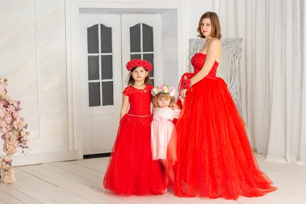 A beautiful woman in a long pink dress in a hall with flowers is photographed with her daughters who have wreaths of flowers on their heads The girls are cute Spring PHOTOSESSION Family