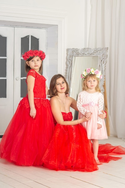 A beautiful woman in a long pink dress in a hall with flowers is photographed with her daughters who have wreaths of flowers on their heads The girls are cute Spring PHOTOSESSION Family