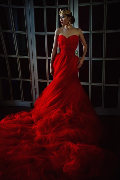 Beautiful woman in long red dress and in royal crown standing near retro door with stainedglass