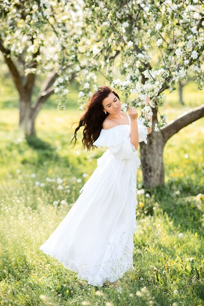 春の庭で長い白いドレスを着た美しい女性。咲く庭の女の子。
