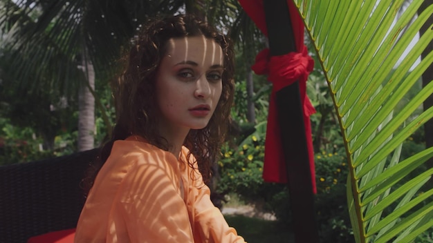 Beautiful woman looking at camera sitting outdoors among palm trees