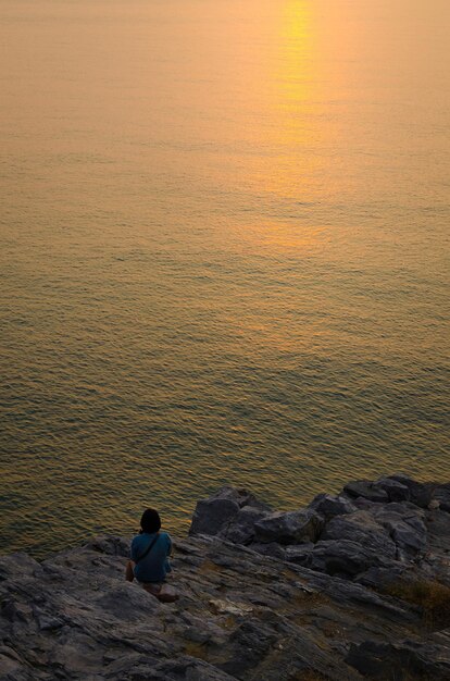 海を見ている美しい女性島のロマンチックな背景の概念で夕日