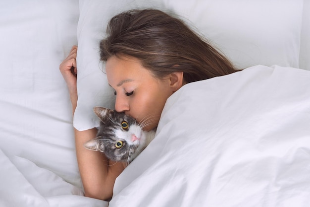 Beautiful woman lying in the bed and kissing her lovely cat Love for cats or people and pets