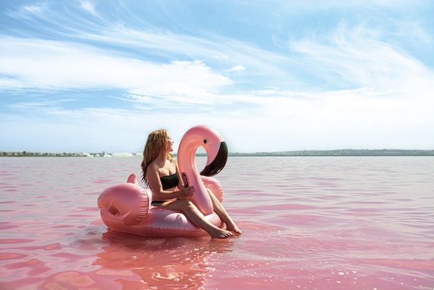 Beautiful woman lying on inflatable float mattress on pink sea