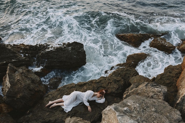 Beautiful woman lying on rocky coast with cracks on rocky\
surface unaltered