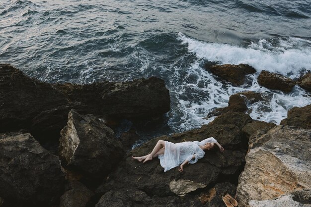 Beautiful woman lying on rocky coast with cracks on rocky\
surface unaltered