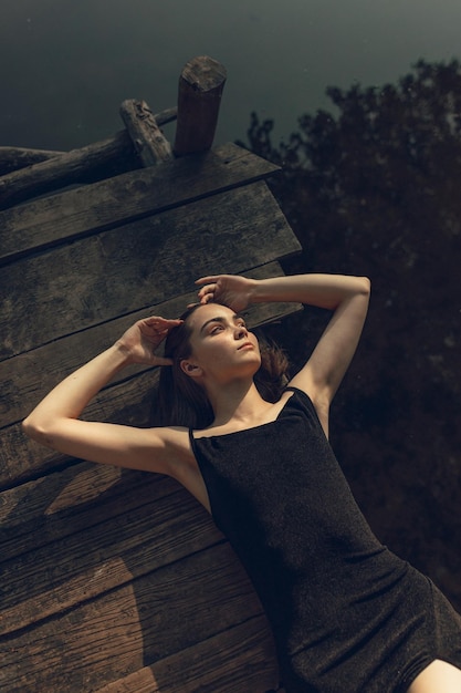 Photo beautiful woman lying on wooden pier near lake in summer while relaxing and looking away