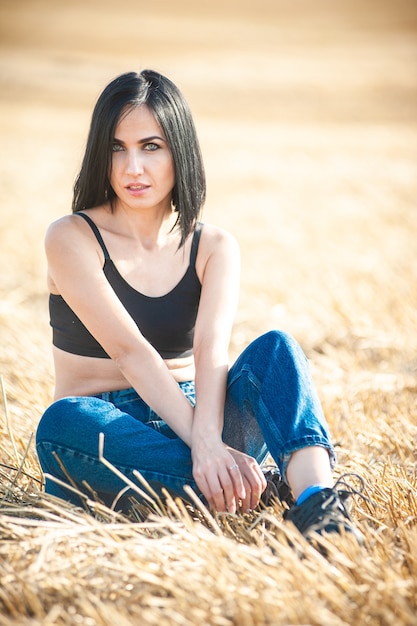 Beautiful woman model wearing summer cotton clothes posing in autumn field with hay stack