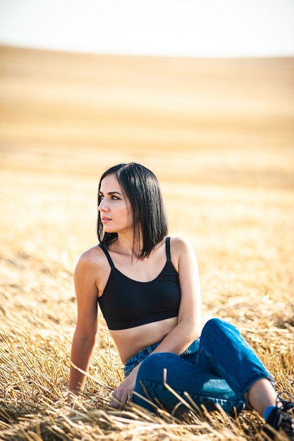 Beautiful woman model wearing summer cotton clothes posing in autumn field with hay stack