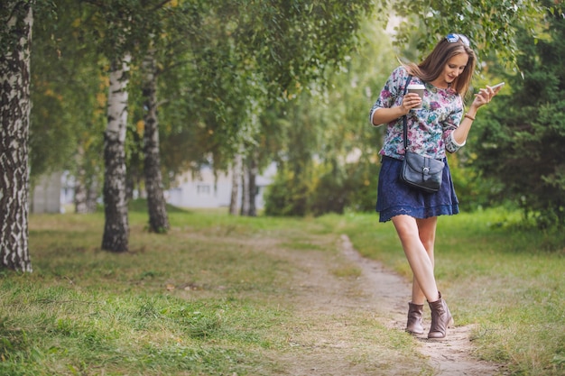 Beautiful woman model with take-away coffee and a telephone in the Park. Style, casual, drink, happiness, Sunny