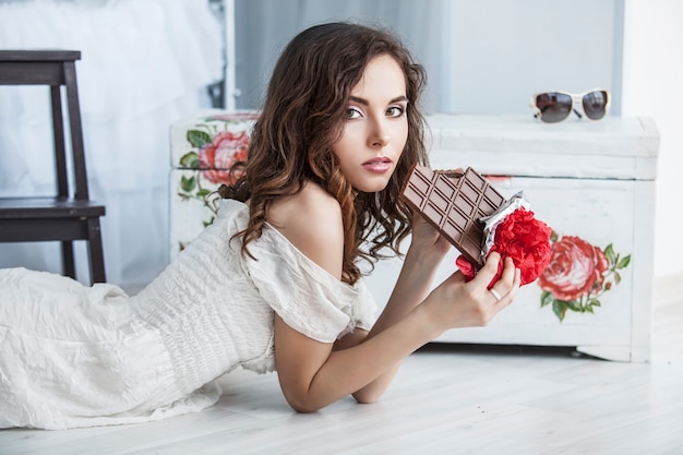 Beautiful woman model with tiles of dark chocolate in hands against bedroom interior