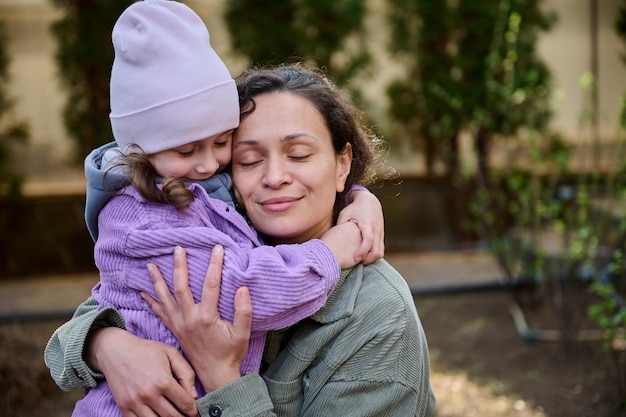 Bella donna madre che abbraccia la sua adorabile figlia mentre stanno insieme nel cortile della sua casa di campagna in una giornata di inizio primavera relazioni familiari giornata di protezione della madre e dei bambini