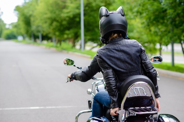 Beautiful woman a motorcycle driver waiting on the road at the evening rear view