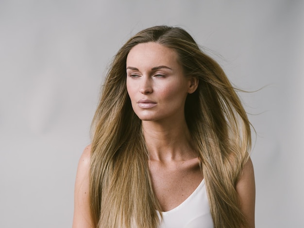 Beautiful woman natural portrait girl with long blonde hair over white gray wall. Studio shot.