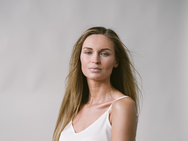 Beautiful woman natural portrait girl with long blonde hair over white gray wall. Studio shot.