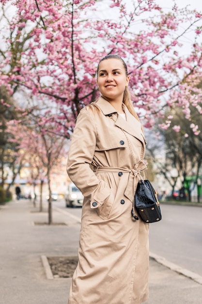 Bella donna vicino agli alberi di sakura. i fiori rosa sbocciano sugli alberi in una strada cittadina. gli alberi fioriscono intorno. concetto di primavera