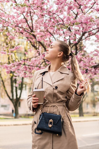 桜の木の近くの美しい女性。街の通りの木々にピンクの花が咲きます。周りに木が咲きます。春の時間の概念