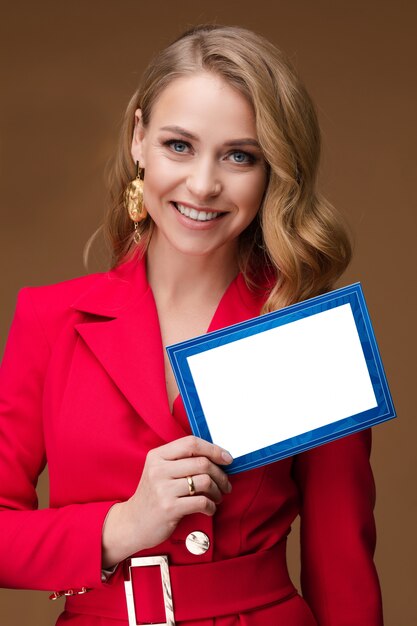 Beautiful woman in office suit smiles and shows a blue and white blank frame board without text, picture isolated