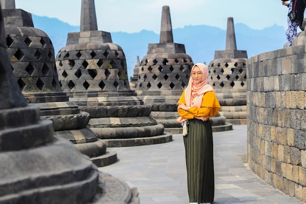 Una bella donna con un vestito arancione posa al tempio di borobudur il tempio più grande del mondo