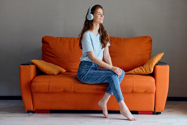 Photo beautiful woman on the orange sofa listening to music with headphones technologies