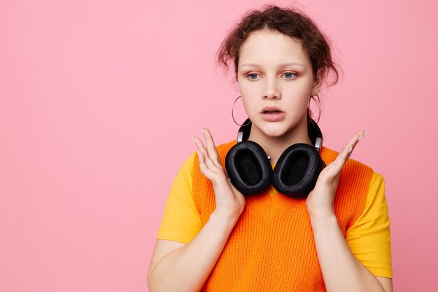 Beautiful woman in an orange sweater headphones music entertainment pink background unaltered