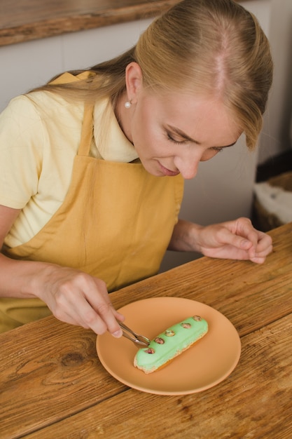 Beautiful woman pastry chef decorates the eclair. Confectionery or cooking courses concept